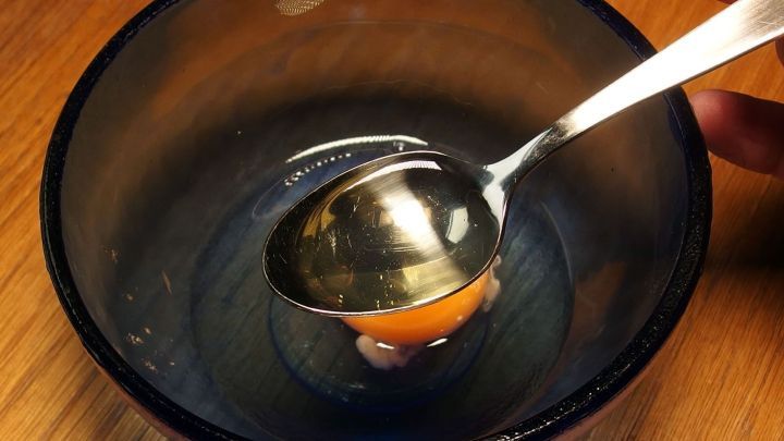 Ein Essl&ouml;ffel mit Eiwei&szlig; wird in einer Sch&uuml;ssel gehalten, um Verbrennungen zu behandeln. Holzuntergrund im Hintergrund.