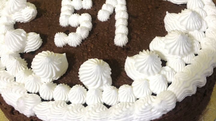 Ein runder Schokoladenkuchen mit Brandyaroma hat eine wei&szlig;e Sahneverzierung und die Zahl 51. Der Kuchen steht auf einem goldenen Teller.