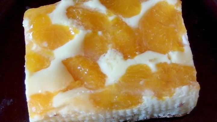 Ein St&uuml;ck K&auml;sekuchen ohne Boden liegt auf einem braunen Teller, garniert mit frischen Mandarinenst&uuml;cken.