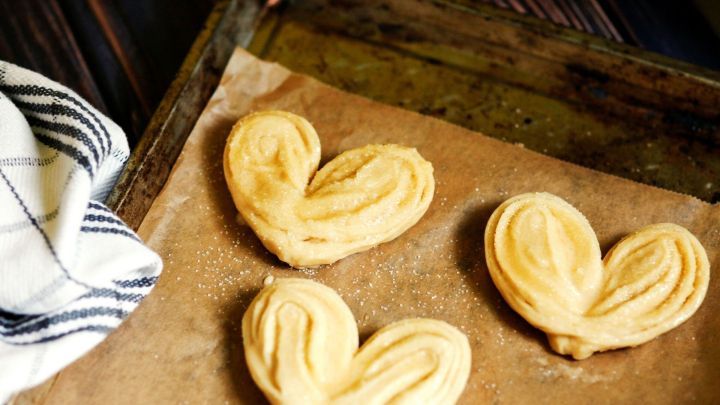 Drei herzf&ouml;rmige Plunderteigst&uuml;cke liegen auf Backpapier in einer Blechtafel, umgeben von einer gestreiften K&uuml;chentuch.