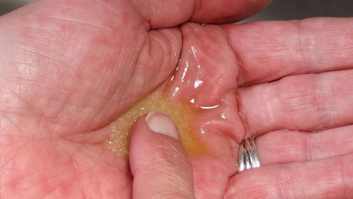 Eine Hand h&auml;lt ein Massagepeeling aus Salz und Oliven&ouml;l, das sanft zwischen den Fingern verteilt wird.