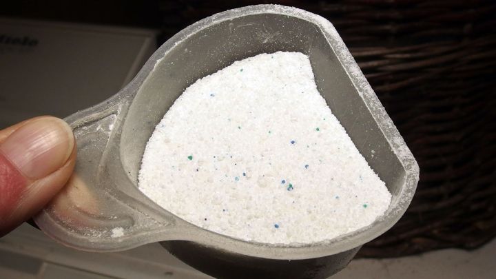 Ein Messbecher mit Waschpulver wird gehalten, w&auml;hrend er &uuml;ber einem Sp&uuml;lbecken schwebt, bereit zum Einf&uuml;llen.