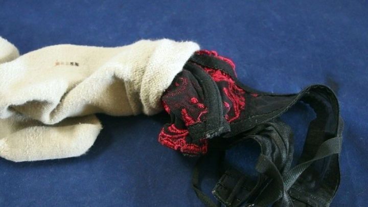 Eine schwarze BH-Tr&auml;ger und ein heller Socken sind miteinander verkn&uuml;pft, auf einem blauen Untergrund platziert, um zu zeigen, was in der Waschmaschine ohne W&auml;schebeutel passieren kann.