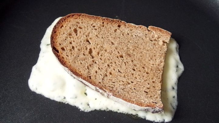 Ein St&uuml;ck K&auml;sebrot br&auml;unt in einer Pfanne, w&auml;hrend der geschmolzene K&auml;se darunter langsam verl&auml;uft.