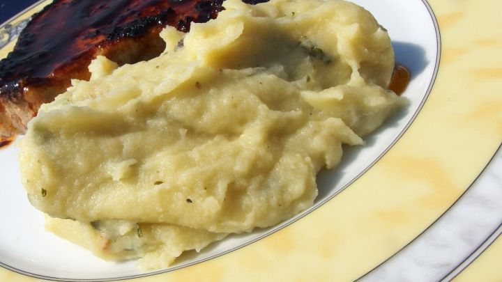 Eine Sch&uuml;ssel Kartoffelbrei liegt auf einem Teller neben einem St&uuml;ck Fleisch, appetitlich angerichtet im Freien.