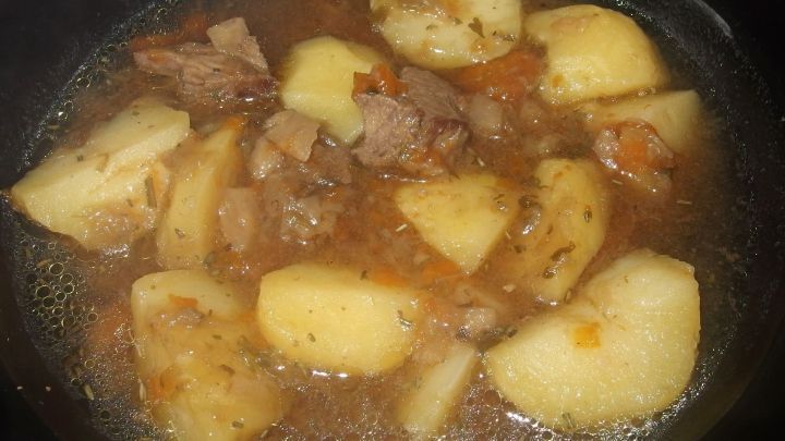 Ein Topf mit Fleischbr&uuml;he wird gekocht, w&auml;hrend Kartoffeln und Fleischst&uuml;cke schwimmen und kr&auml;ftige Farbe annehmen.