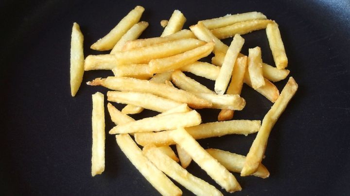 Kalte Pommes liegen verstreut in einer Pfanne und werden weiteren Temperaturen ausgesetzt, um wieder knusprig zu werden.
