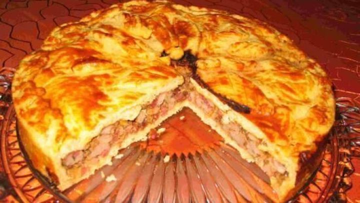 Ein goldener Pie mit Entenbrustf&uuml;llung, ein St&uuml;ck fehlt, ruht auf einem verzierten Glas-Teller auf rotem Tischtuch.