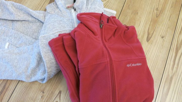 Alte Fleecejacken liegen sauber gefaltet auf einem Holzboden, bereit zur Umwandlung in n&uuml;tzliche Sp&uuml;llappen.