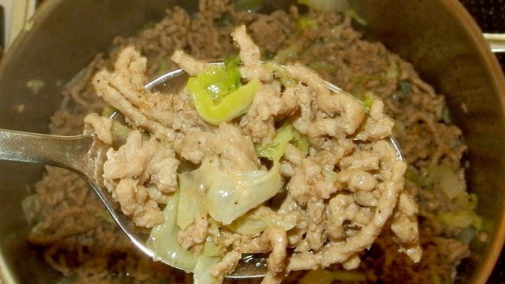 Ein L&ouml;ffel mit gehacktem Fleisch und Chinakohl wird aus einem Topf mit Eintopf genommen, um serviert zu werden.