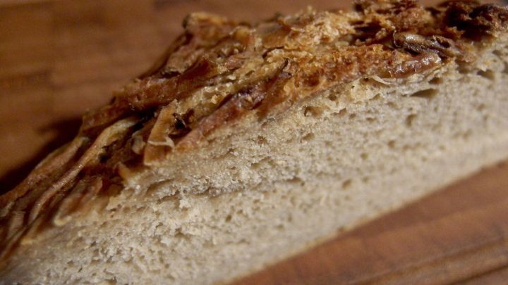 Ein frisches, knuspriges Brot liegt auf einem Holzbrett und zeigt die goldbraune Kruste und die weiche Innenseite.