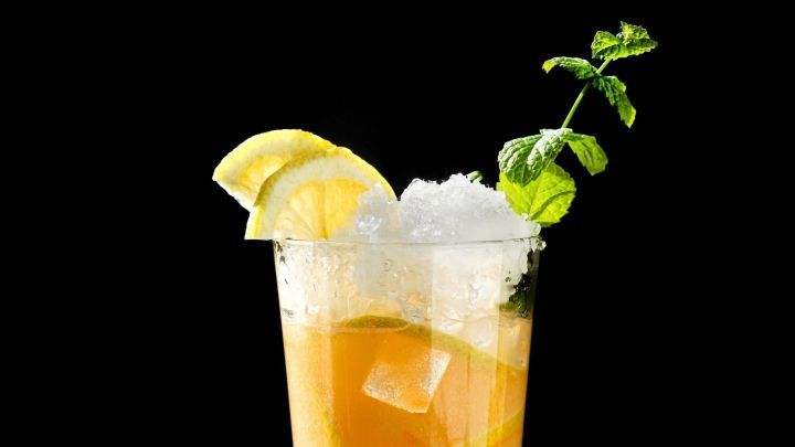 Ein Cocktail mit Malibu steht im Vordergrund, umgeben von Eis und Zitronenscheiben, auf einem dunklen Tisch.