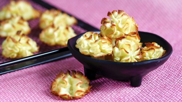 Eine schwarze Sch&uuml;ssel mit knusprigem Kartoffelbrei steht auf einem pinken Tuch, w&auml;hrend einige St&uuml;cke daneben liegen.