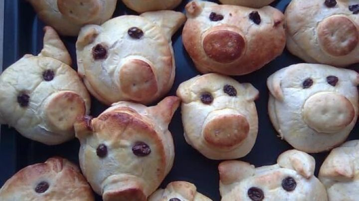 Gl&uuml;cksschweine aus Geb&auml;ck mit Rosinenaugen liegen nebeneinander auf einem Backblech.