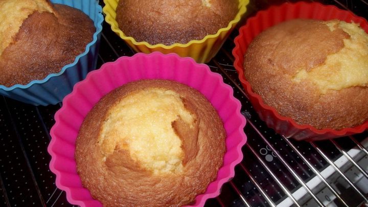 Saftige Orangenmuffins in bunten Silikonf&ouml;rmchen stehen frisch aus dem Ofen auf einem Kuchengitter.