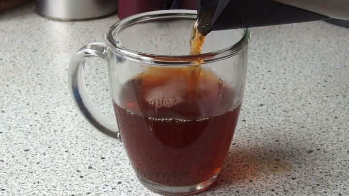 Ein Wasserkocher gie&szlig;t hei&szlig;es Wasser in eine Glaskanne auf einer Arbeitsfl&auml;che, um Tee zuzubereiten.