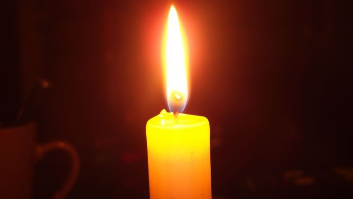 Eine leuchtende, tropffreie Kerze brennt hell in einem dunklen Raum und schafft eine gem&uuml;tliche, warme Atmosph&auml;re.