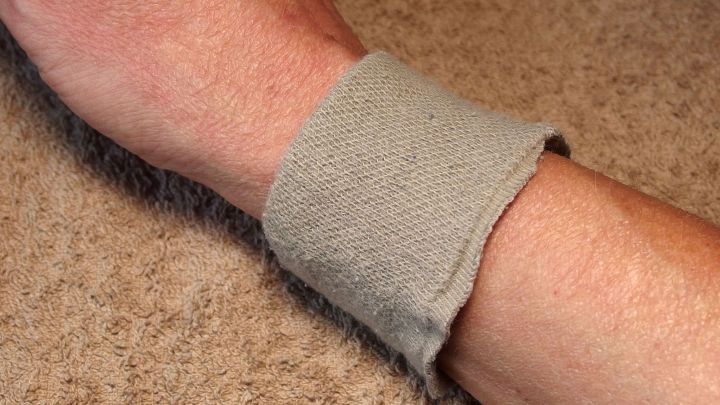 Ein Handgelenk mit einem grauen, weichen Handgelenksschutz liegt auf einem hellen Untergrund, bereit zum Fensterputzen.