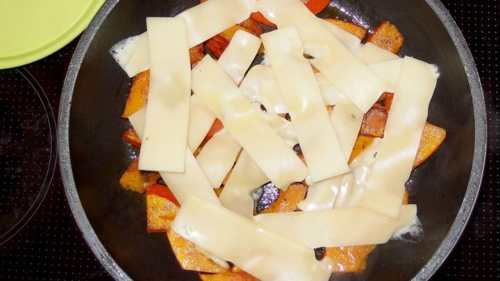 K&uuml;rbisspalten in einer Pfanne mit K&auml;se, der schmelzend darauf liegt, w&auml;hrend sie in der K&uuml;che zubereitet werden.