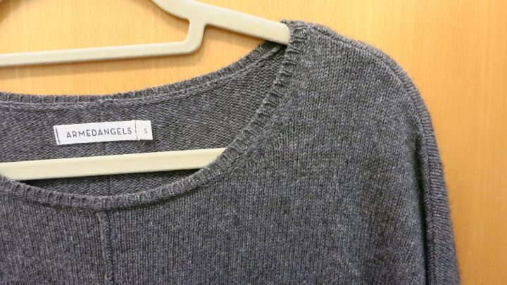 Ein grauer Wollpulli hängt an einem Kleiderbügel, zeigt eine nicht perfekte Passform aufgrund des Einlaufens.