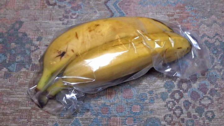 Eine reife Banane liegt in Plastik verpackt auf einem gemusterten Untergrund und bleibt frisch, um den Reifeprozess zu verz&ouml;gern.
