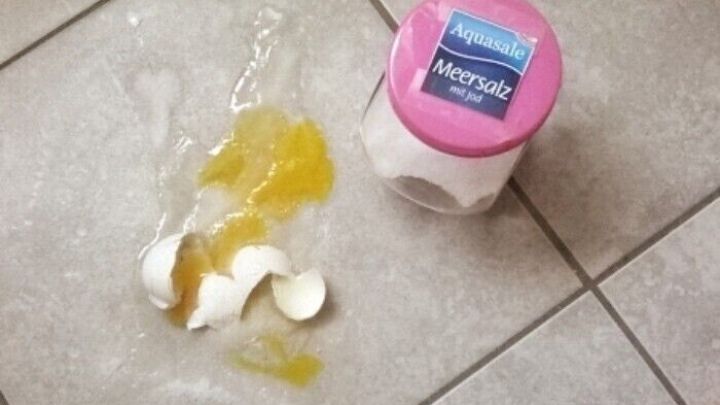 Ein zerbrochenes Ei liegt auf dem Boden neben einer offenen Verpackung mit Salz, bereit zur Reinigung.