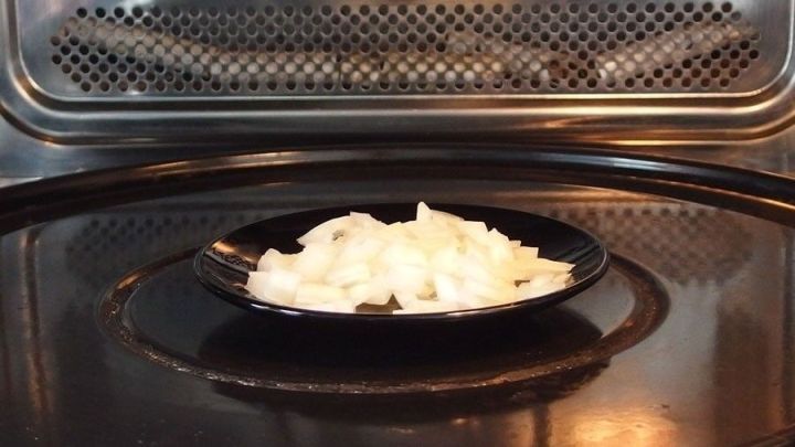 Klein gehackte Zwiebeln liegen auf einem schwarzen Teller in der Mikrowelle und werden zum Vorgaren erhitzt.