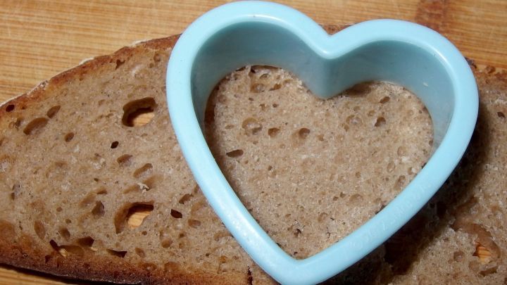 Ein herzf&ouml;rmiger Ausstecher liegt auf einem St&uuml;ck Brot, w&auml;hrend er bereit ist, eine lustige Form auszuschneiden.