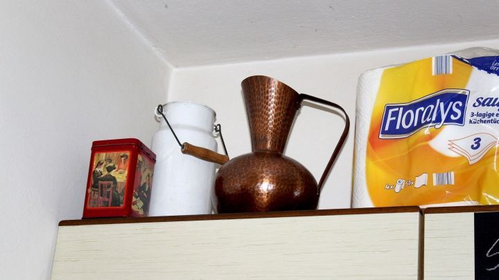 Eine Kupferkanne steht auf einem K&uuml;chenschrank, umgeben von einer wei&szlig;en Milchkanne und Papiert&uuml;chern, die oben ordentlich platziert sind.