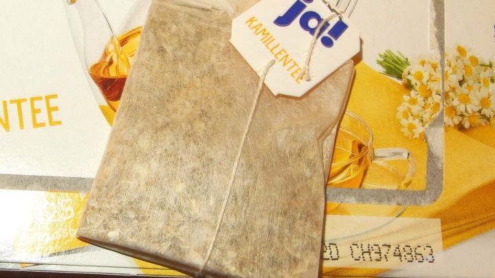 Ein Teebeutel von Kamillentee liegt vor einer Verpackung. Der Teebeutel ist bereit, um bei starken Magenkr&auml;mpfen zu helfen.