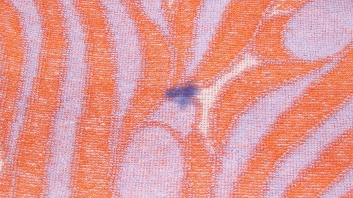 Ein blauer Kugelschreiberfleck liegt auf einem orange gestreiften Tuch, das sauber und ordentlich arrangiert ist.