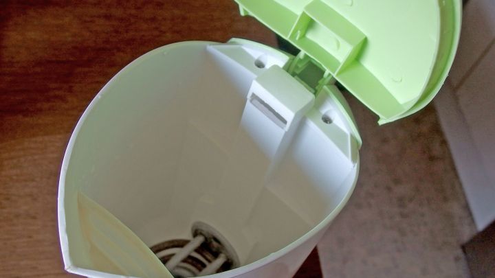 Ein offener Wasserkocher mit erhobenem Deckel und sichtbarem Heizelement steht auf einem Holztisch.