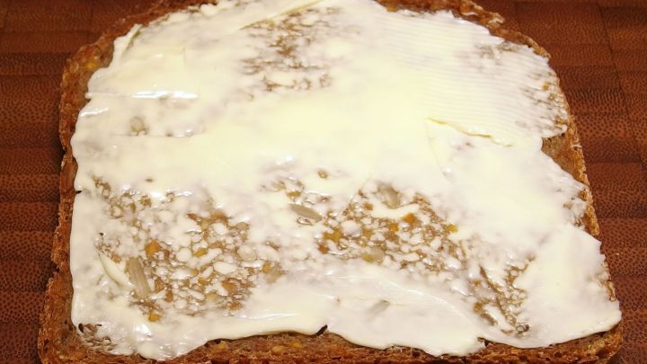 Ein St&uuml;ck Brot aus 630er Dinkelmehl liegt auf einem Holzbrett, bestrichen mit einer cremigen Schicht Butter.