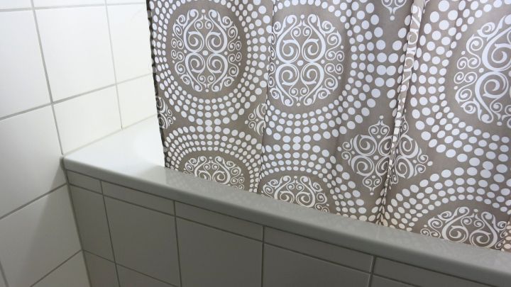 Ein Duschvorhang aus einem modernen Muster h&auml;ngt in einer gefliesten Dusche, um den Raum vor Spritzern zu sch&uuml;tzen.