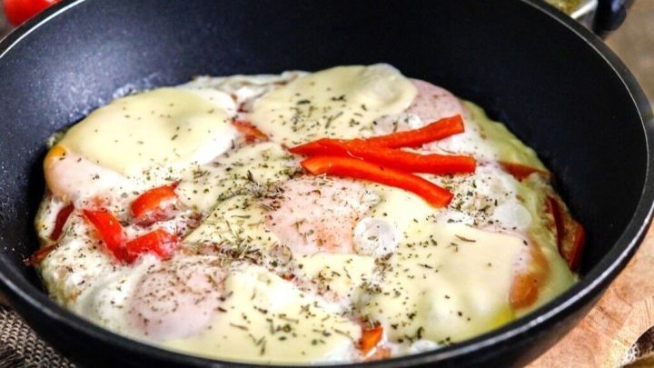 Eine saftige Eierpizza liegt in einer Pfanne, garniert mit Paprika und K&auml;se, vor einer rustikalen Holzoberfl&auml;che.