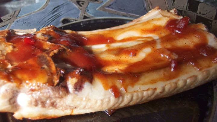 Saftige Spare Ribs liegen auf einem Teller, bedeckt mit w&uuml;rziger BBQ-Sauce, umgeben von einem rustikalen Hintergrund.