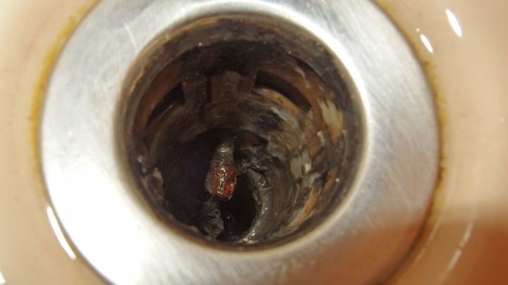 Der Abfluss ist verstopft mit Ablagerungen, umgeben von einem metallischen Rand, in einer Dusche.