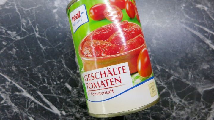 Konservendose mit "GESCH&Auml;LTE TOMATEN" in Tomatensaft, Marke "real quality", auf schwarzer Marmoroberfl&auml;che.
