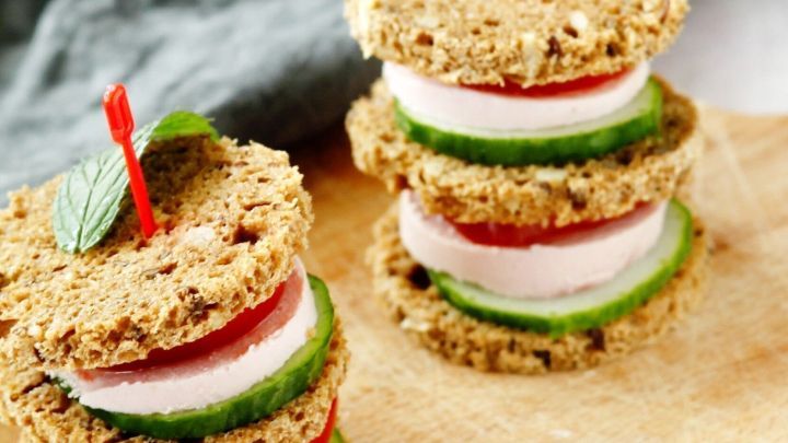 Mini-Burger auf einem Holzbrett, gestapelt mit Gem&uuml;se und H&uuml;hnerbrust, garnierte mit einem Zahnstocher im Hintergrund.