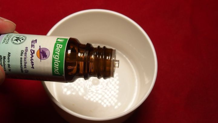 Braune Flasche mit Teebaum&ouml;l wird &uuml;ber eine wei&szlig;e Schale gehalten, w&auml;hrend das &Ouml;l in die Schale tropft.