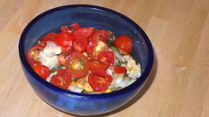 Eine blaue Sch&uuml;ssel enth&auml;lt frisch geschnittene Tomaten, die mit Pesto und anderen Zutaten zubereitet sind.