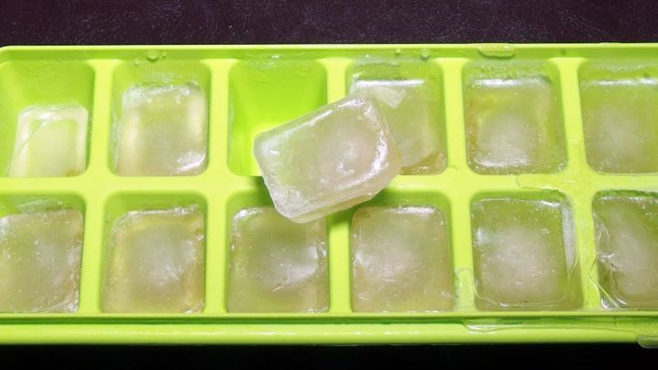 Eisw&uuml;rfel aus Tee liegen in einer gr&uuml;nen Eisw&uuml;rfelschale, einige schmelzen, ideal bei Halsschmerzen.