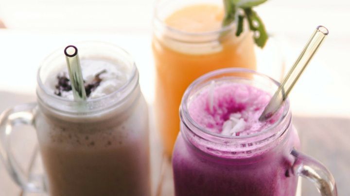 Drei farbenfrohe, alkoholfreie Cocktails stehen auf einem Holztisch und warten auf genussvolle Erfrischung am Strand.