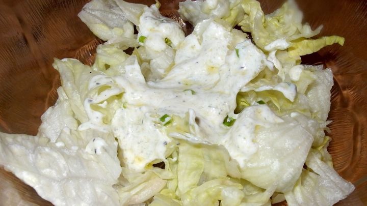 Eine Sch&uuml;ssel mit frischem gr&uuml;nen Salat, der mit einer cremigen Salatsauce vermischt ist, liegt bereit zum Servieren.