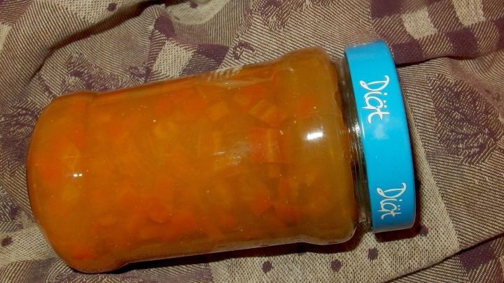 Ein Glas mit Karottenmarmelade steht auf einer karierten Decke, gef&uuml;llt mit leuchtend orangefarbener Marmelade.