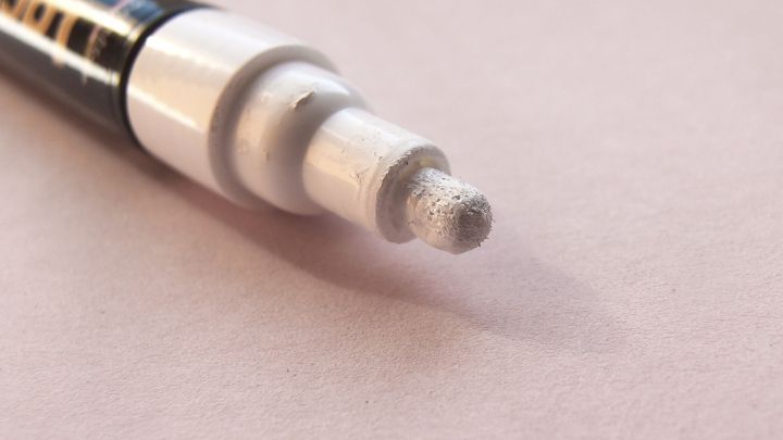 Ein Lackstift liegt auf einem hellen Untergrund und zeigt die abgeschabte Spitze, bereit zum Entfernen mit Nagellackentferner.