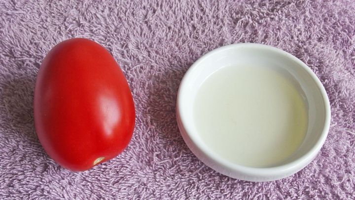 Eine rote Tomate liegt neben einer kleinen Schale mit honigfarbener Fl&uuml;ssigkeit auf einem Tuch, bereit zur Anwendung.