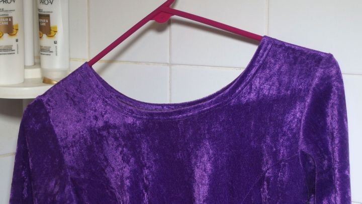 Ein lila, samtiger Stoff h&auml;ngt auf einem Kunststoffb&uuml;gel in einem Badezimmer, um Knitterfalten beim Duschen zu reduzieren.