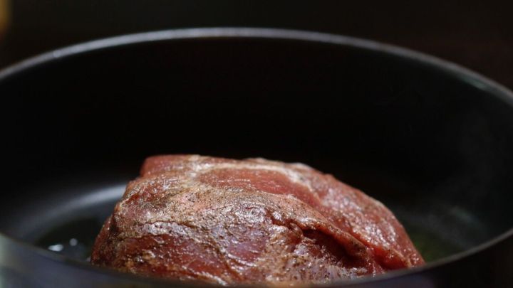 Ein saftiger Rinderbraten liegt in einem Topf, w&auml;hrend er auf dem Herd gart und eine appetitliche Br&auml;unung annimmt.