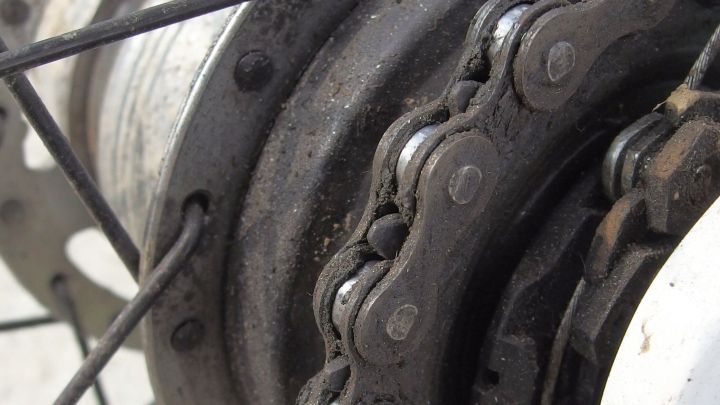 Ein schmutziger, &ouml;liger Fahrradzahnkranz mit einer abgenutzten Kette, die in einer Werkstattumgebung steht.